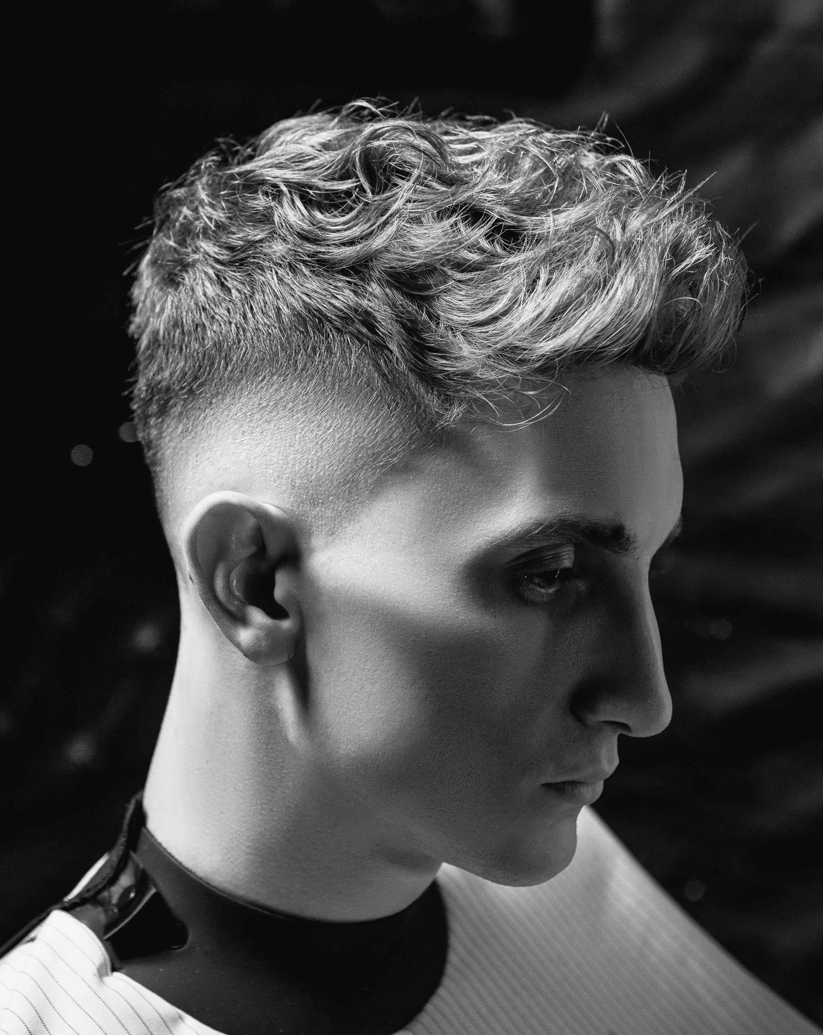 Zwart-witportret van een man met krullen bovenop en een strakke skin fade aan de zijkant