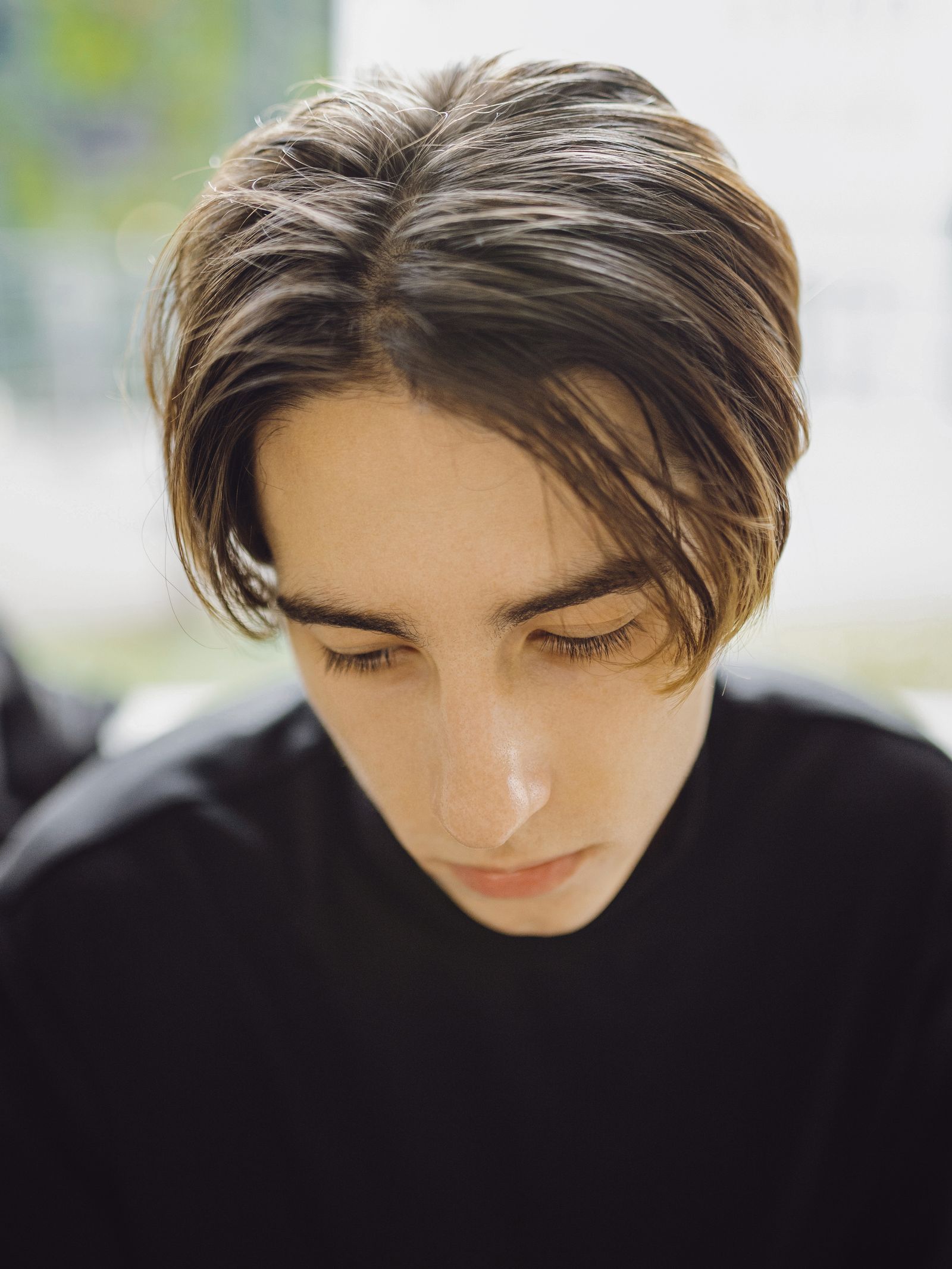 Jonge man met halflang haar en een middenscheiding die het haar als gordijnen langs zijn gezicht laat vallen