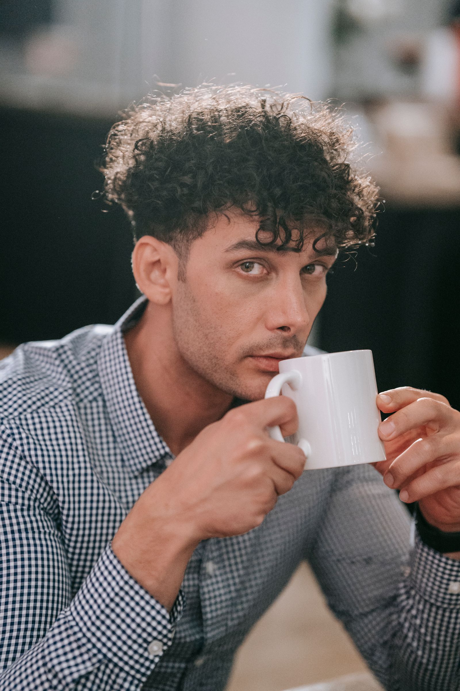 Man met korte krullen bovenop en kortere zijkanten, met een kop koffie