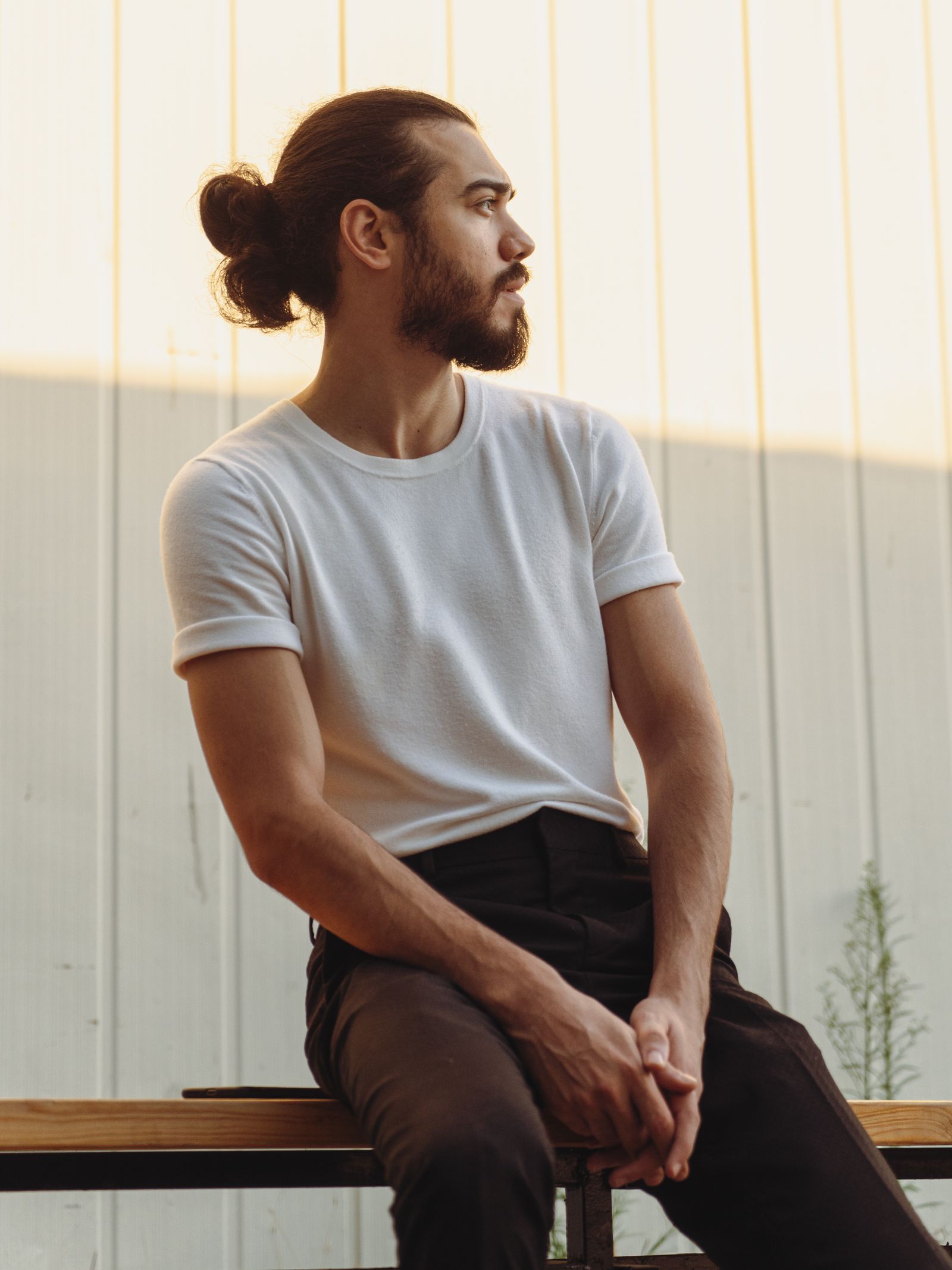 Man met baard en lang haar in een man bun, zittend op een bank