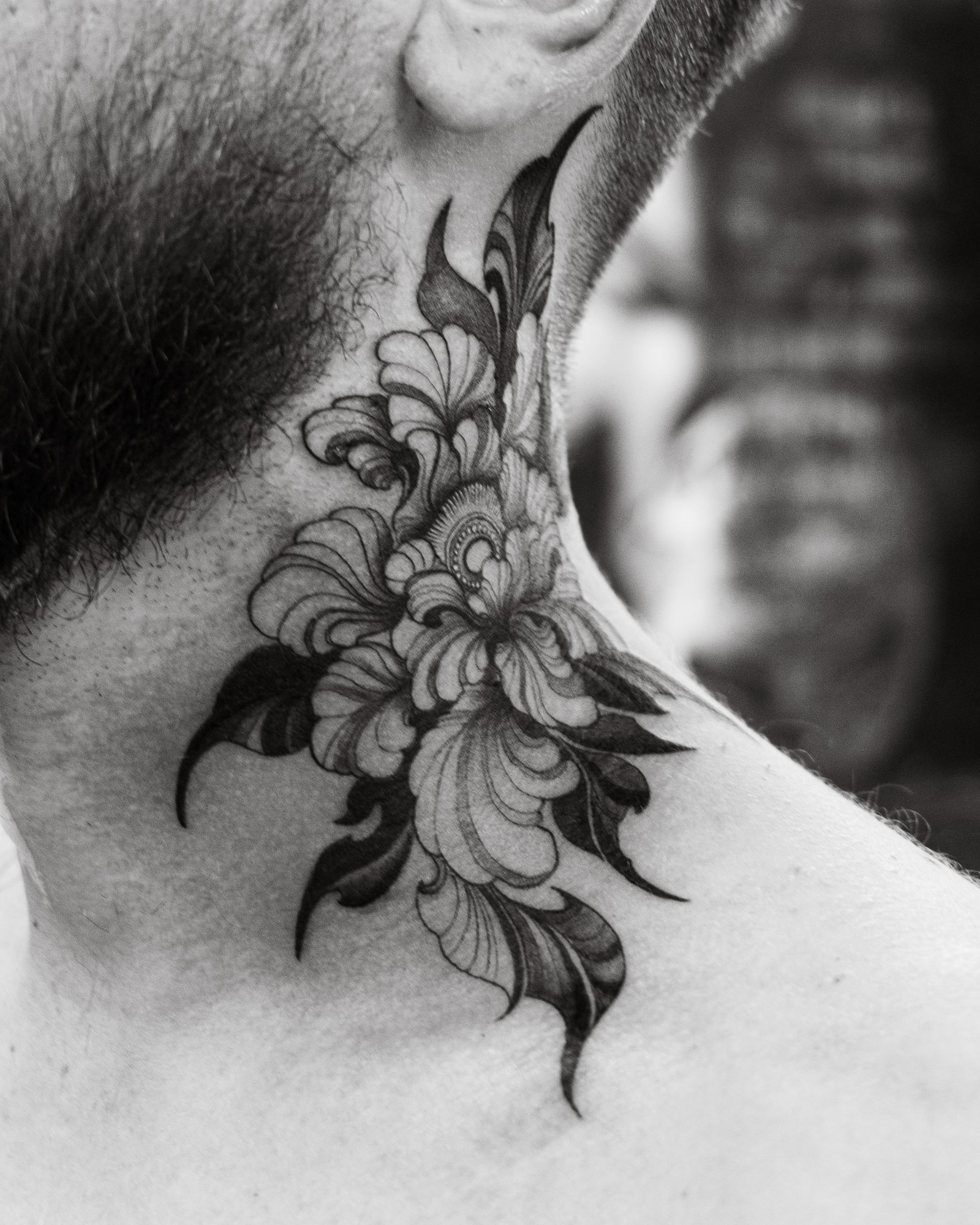 Zwart-witfoto van een bloementattoo in zwarte inkt aan de zijkant van de nek van een man