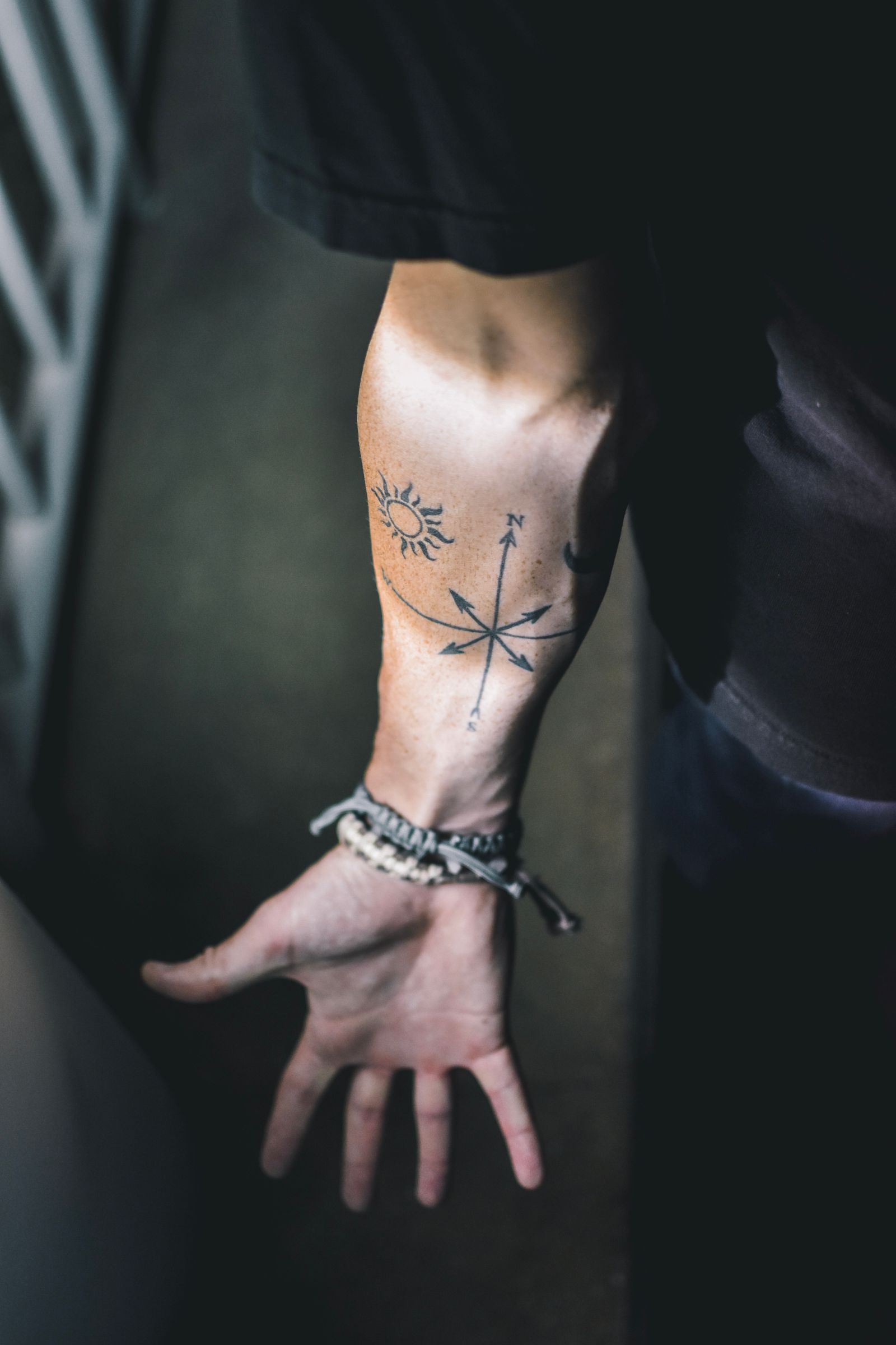 Onderarm van een man met kleine fine line tattoos van een kompasroos en een zonnetje, met armbandjes om de pols