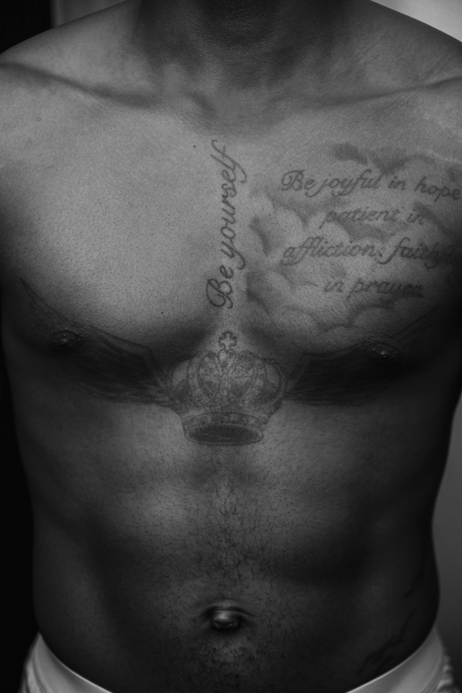 Zwart-witfoto van de borst van een man met getatoeëerde teksten in sierlijk schrift