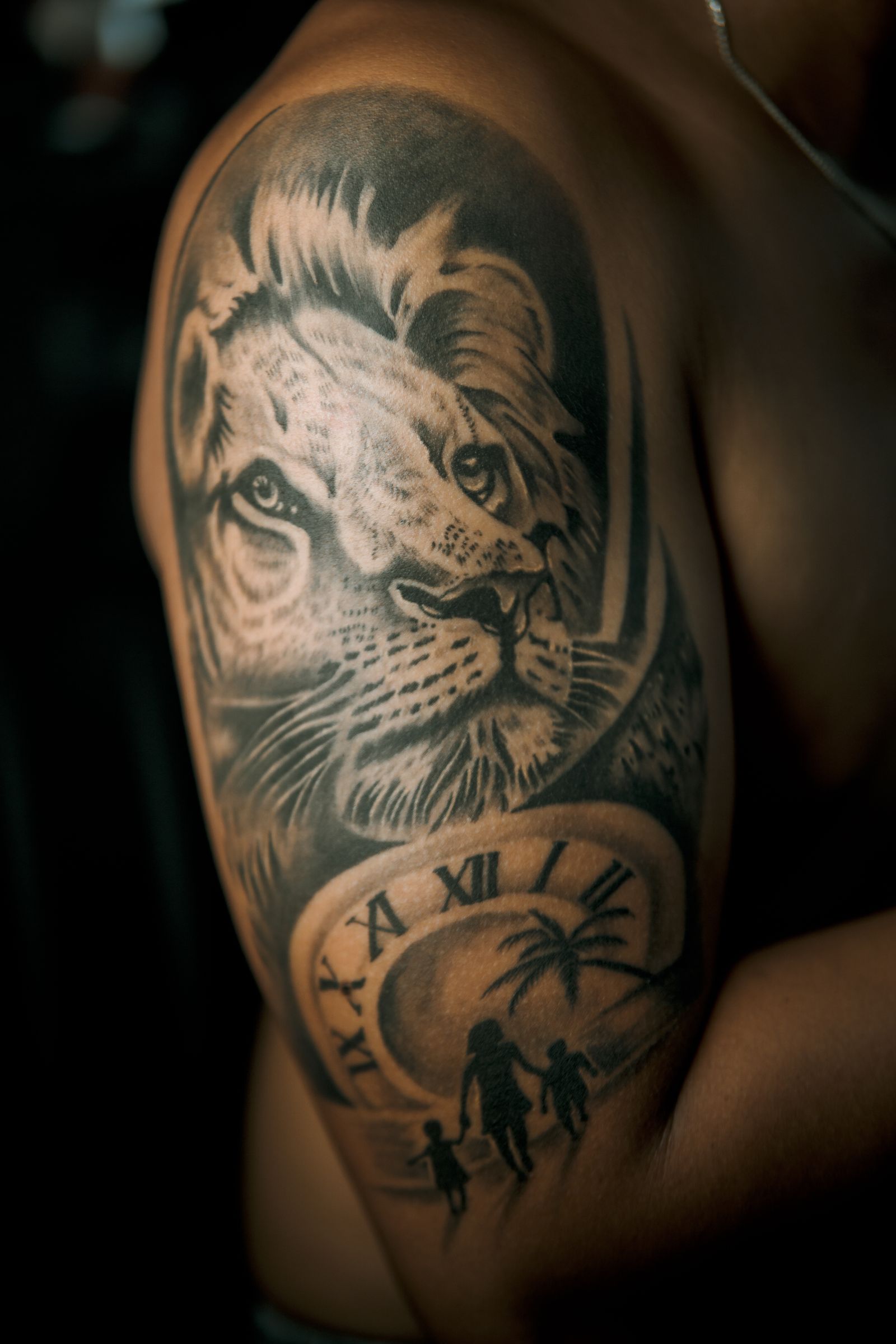 Bovenarm en schouder van een man met een realistische tattoo van een leeuwenkop boven een klok